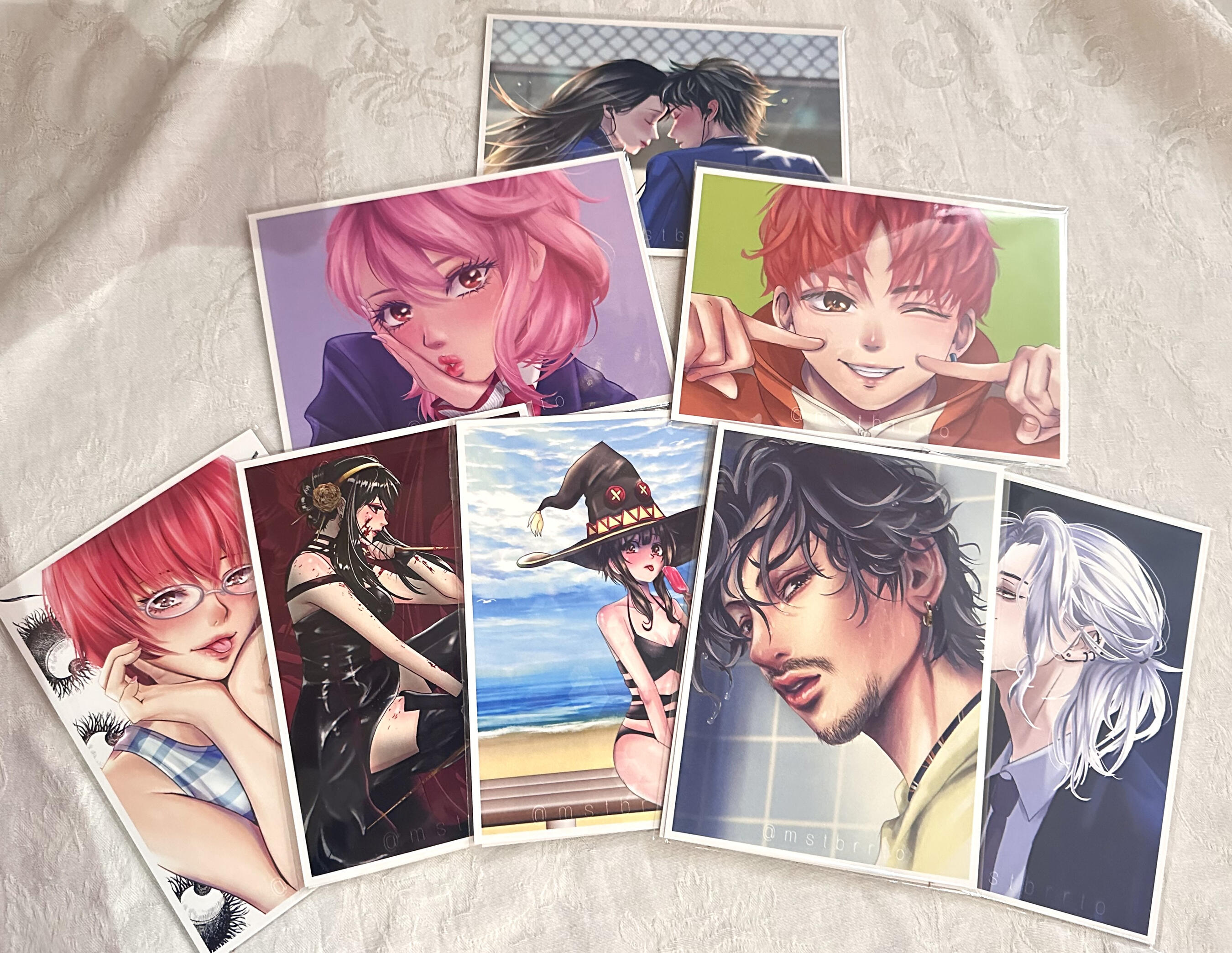 5x7 anime art print collection A selection of colorful anime‑inspired art prints displayed on a white cloth background.